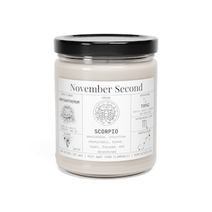 May include: A beige soy wax candle in a glass jar with a black lid. The label reads "November Second" and features zodiac details for Scorpio, including birth flower, birthstone, and traits. The candle is made with natural soy wax.