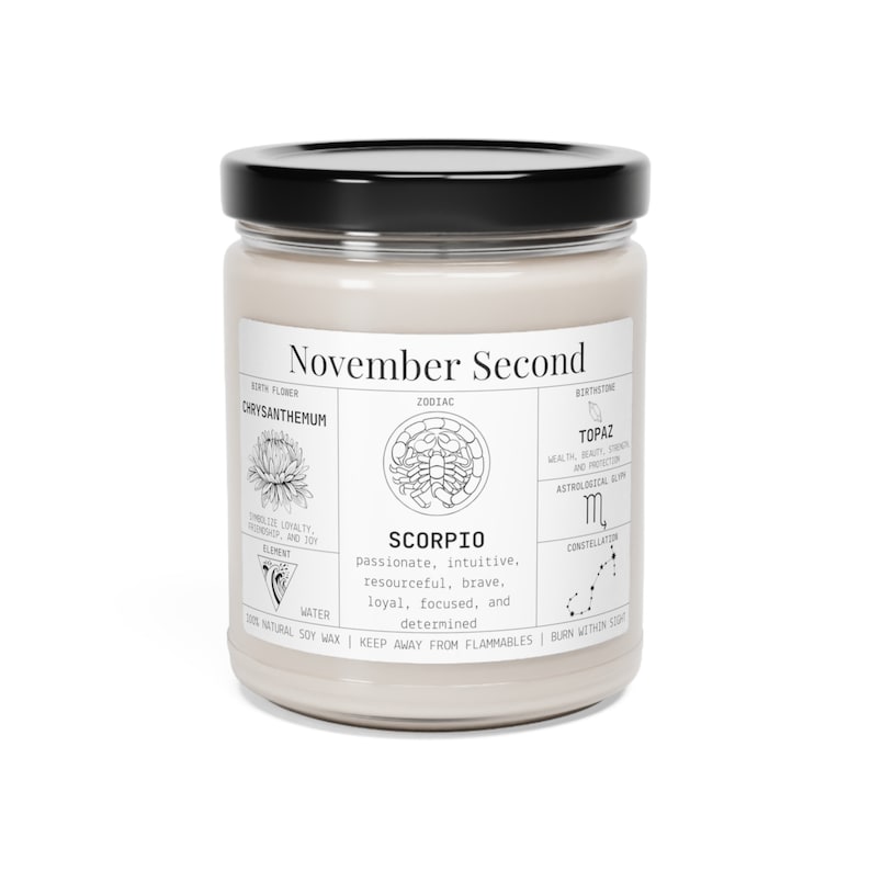 May include: A beige soy wax candle in a glass jar with a black lid. The label reads "November Second" and features zodiac details for Scorpio, including birth flower, birthstone, and traits. The candle is made with natural soy wax.