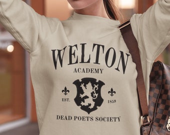 May include: A beige sweatshirt with the text "Welton Academy" and "Dead Poets Society" printed on the front. The sweatshirt also features a black and white crest with a lion and the text "Est. 1859".
