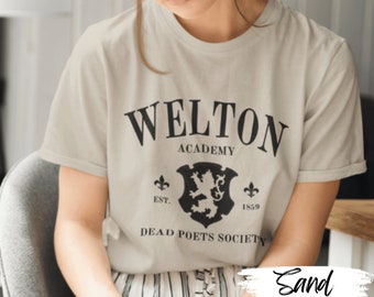 Könnte beinhalten: Ein sandfarbenes T-Shirt mit einem schwarzen Aufdruck, der "Welton Academy" und "Dead Poets Society" lautet. Der Druck enthält auch ein Wappen mit einem Löwen und dem Jahr 1859.