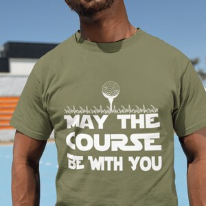 May include: A green t-shirt with a white golf ball graphic and the text "May the Course Be With You".