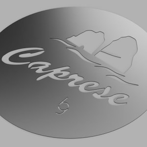 Può includere: Un tagliapasta rotondo in argento con un disegno di due isole e la parola "Caprese" in un font corsivo.