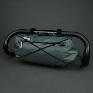 Könnte beinhalten: Eine tealfarbene Lenkertasche mit schwarzem Reißverschluss und elastischen Kordeldetails, montiert an einem schwarzen Fahrradlenker. Auf der Tasche ist der Markenname "KREIS" aufgedruckt. Auf dem Lenker steht auch das Wort "CONTACT".
