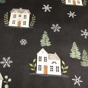 May include: Black fabric featuring a repeating pattern of white houses, green pine trees, and white snowflakes. The houses have brown doors and are surrounded by green and yellow foliage. The trees are green, and the snowflakes are white.