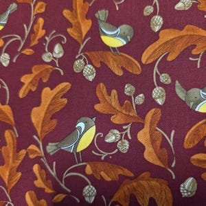 May include: A burgundy fabric with a repeating pattern of yellow birds, brown acorns, and orange leaves.