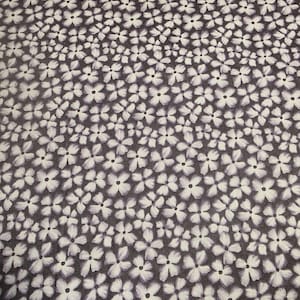 May include: A dark purple fabric with a white floral pattern. The flowers are small and have five petals.