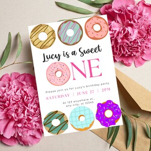 May include: A white invitation card with a pink and black donut theme. The text reads "Lucy is a Sweet ONE". The invitation includes details for a birthday party on Saturday, June 27th at 2 PM.