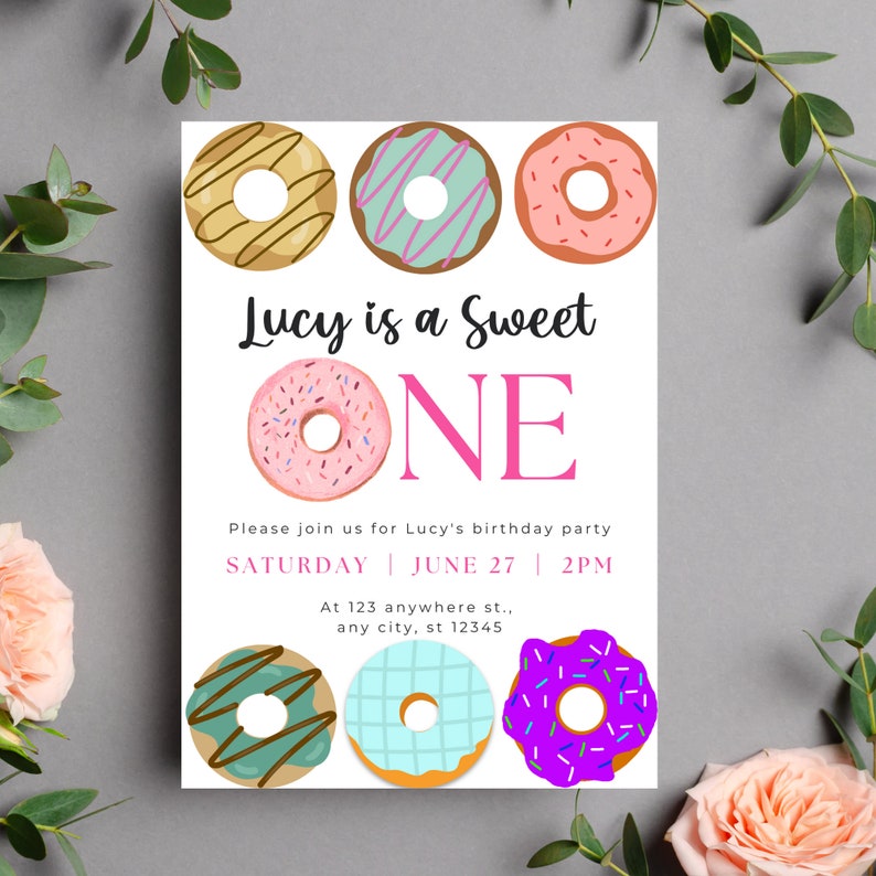 May include: A donut-themed birthday party invitation for a girl turning one year old. The invitation features colorful donuts with sprinkles and the text "Lucy is a Sweet ONE". The invitation also includes the date and time of the party: "SATURDAY JUNE 27 2PM".