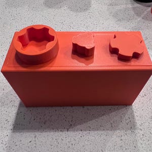 May include: A red rectangular box with three different shaped holes on the top. The holes are shaped like a star, a heart, and a circle.