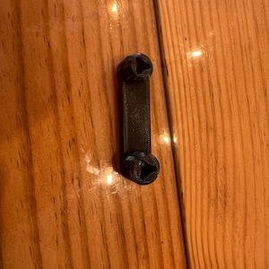 May include: A black plastic 3D printed object with two small holes on each end.