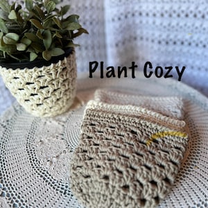 Puede incluir: Un acogedor de plantas de ganchillo en crema y marrón, con un juego de posavasos a juego. El acogedor de plantas envuelve una maceta negra con una planta verde. El texto "Plant Cozy" se muestra en negro.