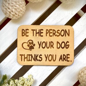 May include: Wooden sign with the text "Be the person your dog thinks you are."  The sign has a heart with a paw print inside.