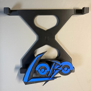 May include: Black and blue wall-mounted holder with a stylized logo. The holder features a geometric design with a central hourglass shape and two upper arms. The logo is in blue and black, with a modern, angular font.