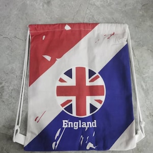 May include: A white drawstring bag with a red, white and blue design. The bag features a circle with the Union Jack flag and the word "England" printed below it.