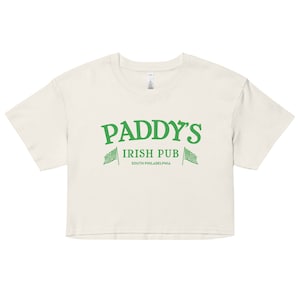 May include: Cream-colored crop top with the text "PADDY'S IRISH PUB SOUTH PHILADELPHIA" in green. The design includes two green flags. The shirt has a crew neck and short sleeves.