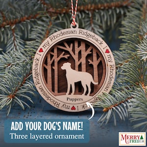 May include: A wooden Christmas ornament featuring a silhouette of a Rhodesian Ridgeback dog standing in a forest. The ornament is three-layered and has the text "I ❤ my Rhodesian Ridgeback. I ❤ my Rhodesian Ridgeback." around the edge. The text "Puppers" is written below the dog.