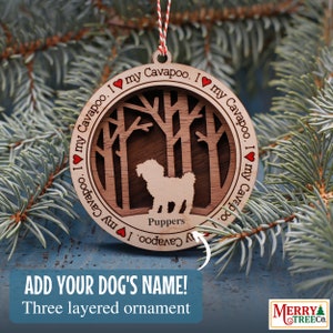 Puede incluir: Un adorno navideño de madera con la silueta de un perro Cavapoo en una escena de bosque. El adorno es de tres capas y tiene el texto "Amo a mi Cavapoo. Amo a mi Cavapoo." alrededor del borde. El texto "Puppers" está debajo de la silueta del perro.