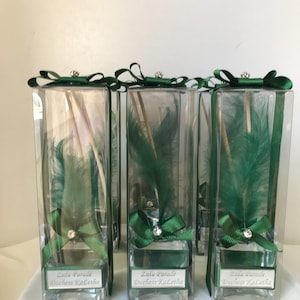 Può includere: Tre bottiglie di vetro trasparente con piume verdi e fiocchi di nastro verde. Ogni bottiglia ha un'etichetta con la scritta "Zulu Parade Duchess Kalettha".