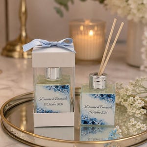 Può includere: Due diffusori di fragranza in vetro quadrato con tappi argentati ed etichette floreali azzurre. Uno è all'interno di una scatola bianca con un nastro azzurro. Le etichette riportano il testo S.Cresima di Emanuele 17 Ottobre 2026.