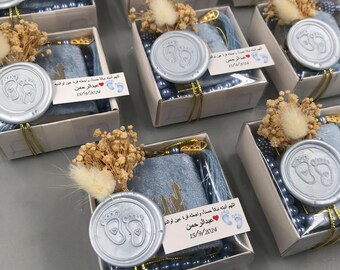 May include: A set of blue gift boxes with a silver seal featuring a pair of baby footprints. Each box contains a small blue prayer rug, a set of blue prayer beads, and a white card with Arabic text and the date "15/9/2024".