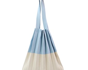 May include: A pleated tote bag in light blue and off-white. The bag has a long, matching strap for carrying over the shoulder. The bag's design features vertical pleats, creating a textured appearance. The bag is made of a soft, flexible material.