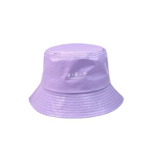 Puede incluir: Un sombrero de pescador lavanda con un acabado ligeramente brillante. El sombrero presenta un pequeño gráfico blanco y el texto "FLAVOURS DON'T LIE" en blanco. Tiene una corona redondeada y un ala inclinada hacia abajo.