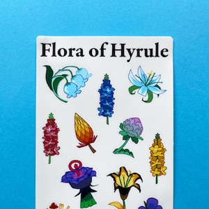 May include: A sticker sheet featuring colorful illustrations of various flowers, labeled "Flora of Hyrule." The designs include bluebells, blue spikes, and yellow lilies. The artist's handle, @flabbermouse, is printed at the bottom.