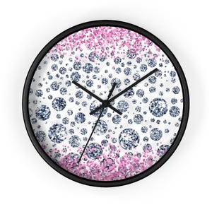 Puede incluir: Reloj de pared redondo con marco negro. La esfera presenta un fondo blanco con un patrón de diamantes azules y purpurina rosa. Las manecillas negras indican la hora.
