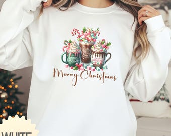 May include: White sweatshirt featuring a festive graphic of three mugs of hot chocolate with whipped cream, candy canes, and the words "Merry Christmas." The mugs are green, brown, and teal. A holiday-themed apparel item.