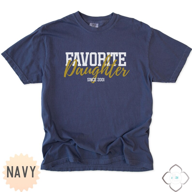 Puede incluir: Camiseta azul marino con el texto "FAVORITE DAUGHTER" en letras blancas en bloque sobre la palabra "Daughter" en escritura dorada. El texto "SINCE 2001" est&aacute; debajo. La camiseta es de estilo casual.