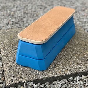 May include: A blue wooden footrest with a cork top. The footrest is rectangular with a light blue base and a natural cork surface. The footrest is designed to provide comfort and support.