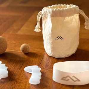 May include: A set of white silicone toe separators, a white silicone ring with a mountain logo, two brown cork balls, and a white canvas bag with a mountain logo.