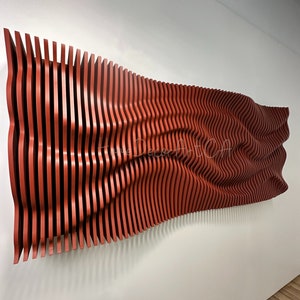 Puede incluir: Una gran pieza de arte mural abstracto con un diseño ondulado. Está hecha de listones de madera verticales y espaciados uniformemente, pintados en un color marrón rojizo cálido. La obra está montada en una pared blanca.