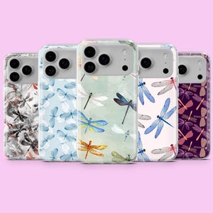 May include: A collection of five phone cases with dragonfly designs. The cases feature various color schemes, including blue, white, orange, and purple dragonflies on different backgrounds. The cases are displayed against a pink background.