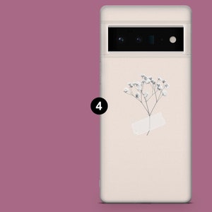 May include: A white phone case with a small white flower and a white paper tag. The phone case has a black camera lens.