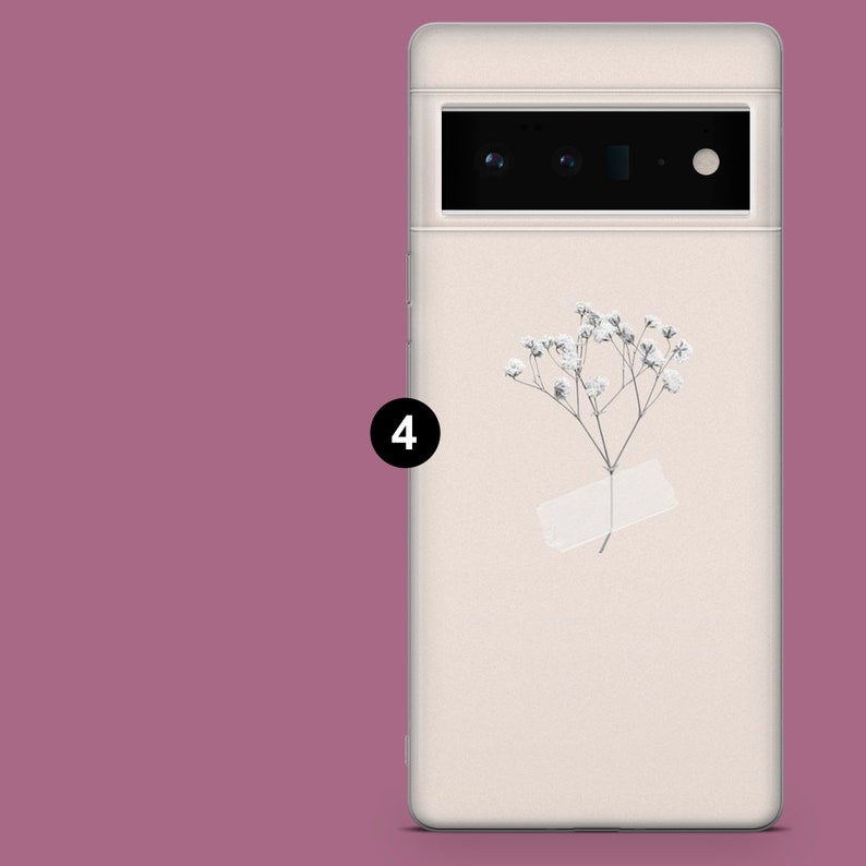 May include: A white phone case with a small white flower and a white paper tag. The phone case has a black camera lens.