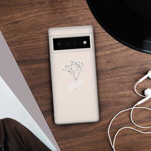May include: A white phone case with a delicate pressed flower design and a black camera lens.