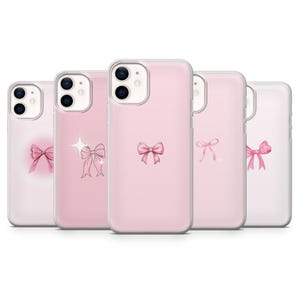 Könnte beinhalten: Fünf rosa Handyhüllen, jede mit einem anderen Design einer rosa Schleife. Die Schleifen variieren im Stil, einige mit Aquarelleffekten und andere mit Glitzer. Die Hüllen bestehen aus einem transparenten, schützenden Material.