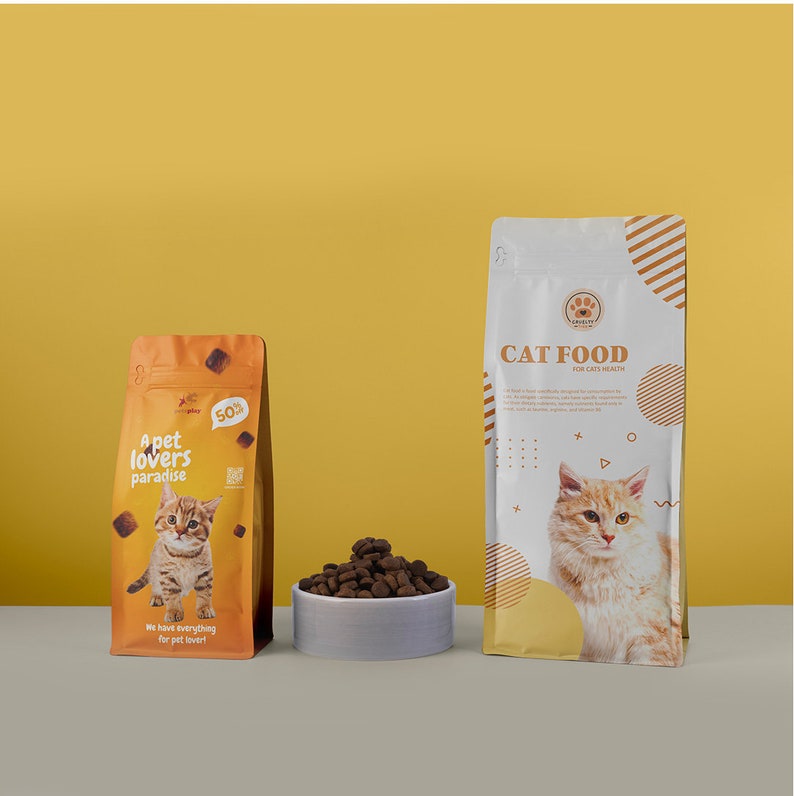 May include: Two bags of cat food and a bowl of kibble are displayed against a yellow background. One bag is orange with a kitten graphic and the text "A pet lovers paradise". The other bag is white with "CAT FOOD" and a cat graphic. The bowl is light gray.