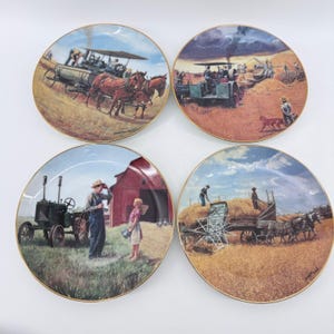 Puede incluir: Cuatro platos de colección redondos de cerámica con bordes dorados, cada uno con escenas rurales detalladas. Las ilustraciones representan actividades agrícolas históricas, incluyendo maquinaria tirada por caballos, un tractor verde y un granero rojo.