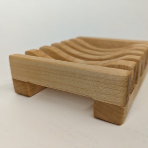 May include: A wooden soap dish with a wavy design. The dish is made of light wood and has a natural finish.