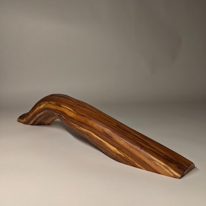 May include: A wooden handle with a curved shape and a natural wood grain pattern. The handle is made of a light brown wood with darker brown streaks.