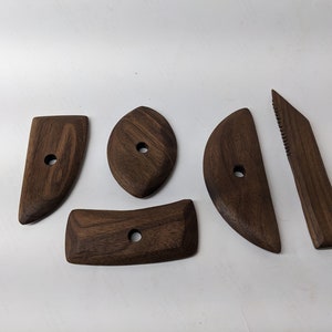 May include: Five wooden tools for sculpting clay, made of dark brown walnut wood. The tools have different shapes, including a curved blade, a rounded edge, and a flat edge.