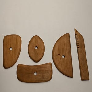 May include: Five wooden tools for sculpting clay. The tools are made of light brown wood and have a smooth finish. Each tool has a different shape and size, including a rounded shape, a teardrop shape, a half-circle shape, a curved shape, and a long, thin shape.
