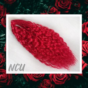 May include: A bundle of bright red curly hair extensions. The hair is arranged in a loose, wavy style. The hair is long and thick, and it appears to be in good condition.