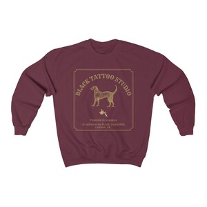 May include: Burgundy sweatshirt with a gold graphic of a dog holding a tattoo machine. The graphic says "Black Tattoo Studio" and "Trained in Azkaban 12 Grimmauld Place, Islington London, UK."