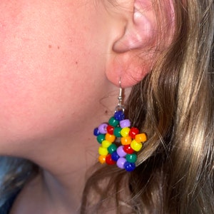 May include: Rainbow star-shaped beaded earrings. The earrings are made with small, colorful beads in a rainbow pattern. The beads are strung on silver wire.