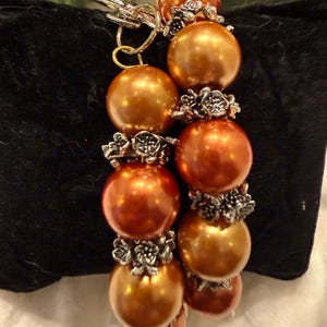 May include: A bracelet featuring two strands of lustrous, metallic copper-colored spherical beads. Each bead is separated by small, intricate silver-toned metal spacers shaped like clusters of tiny flowers. The bracelet includes a silver-toned toggle clasp.