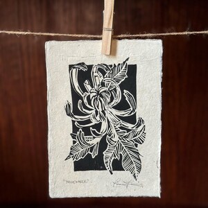 K&ouml;nnte beinhalten: Schwarz-wei&szlig;er Linolschnitt einer Chrysanthemenbl&uuml;te mit dem Text "November" unten.