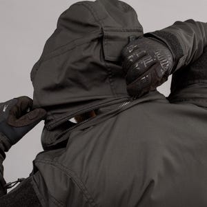 May include: Black hooded jacket with a zipper closure. The jacket has a pocket on the hood and is being zipped up by a person wearing black gloves. The jacket appears to be made of a durable, weather-resistant material.